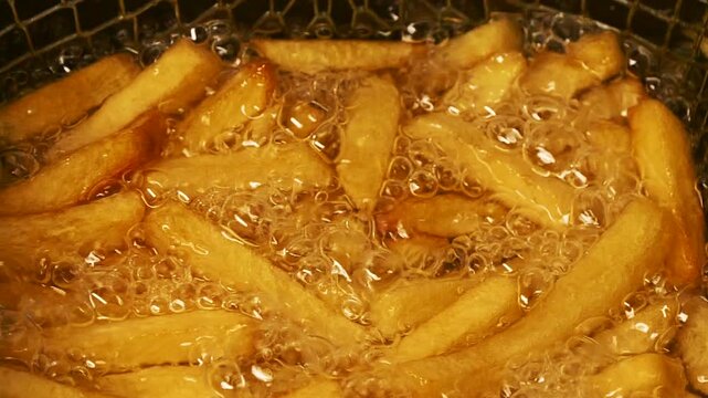 Close-up slow motion fried crispy potato wedges deep frying in oil. French fries