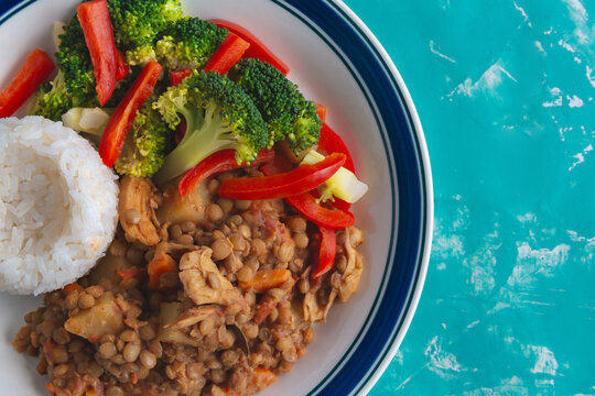 Plates hold lentils, rice, and vibrant veggies. Broccoli and red peppers add color and freshness. Dish rests on a textured blue surface. Serving suggests healthy, balanced meal. Appeal ideal for food