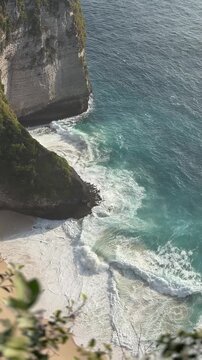 Aerial view of a rocky coastline with turquoise waters and white sandy beach. Waves crash against the cliffs, creating a serene natural landscape.