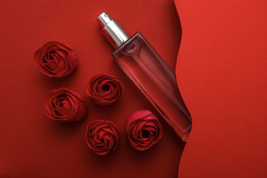Perfume bottle with rose buds on a red wavy layered background. Creative layout. Romantic, Love concept