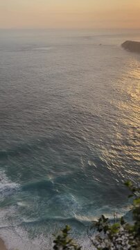 A serene ocean view at sunset, with gentle waves lapping against the shore. The sky is painted in warm hues of orange and pink, reflecting on the water.