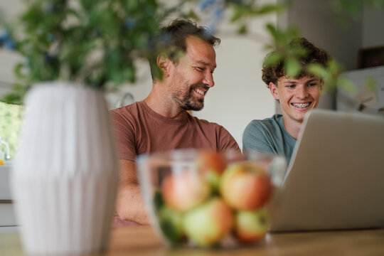 Father supporting teen son with online learning at home.