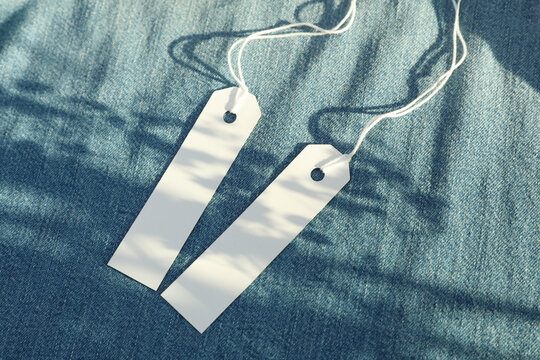 White blank tags on blue denim background with natural sunlight