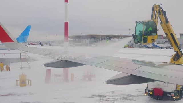 Ground crew spraying deicing fluid on airplane wing during snowy winter weather at airport.