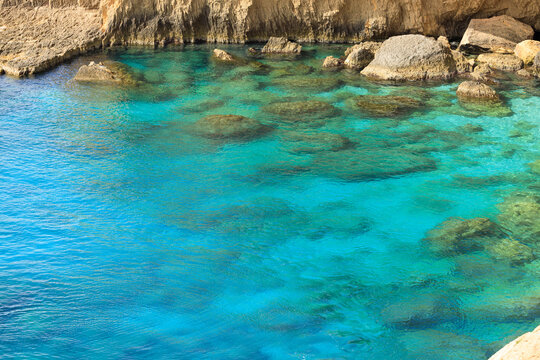 Crystal clear turquoise sea water meeting a rugged rocky coastline under bright summer sunlight