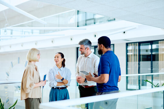 Diverse business professionals discussing work, exchanging ideas, and communicating in a contemporary corporate building environment