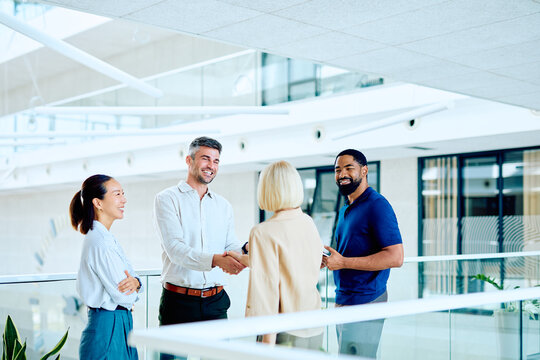 Group of multi-ethnic business people standing in a modern office building, two smiling and shaking hands, symbolizing agreement and partnership