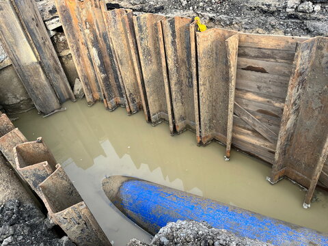 Steel and wooden support wall near a sewage manhole to prevent soil from collapsing on the blue drain pipe of large diameter