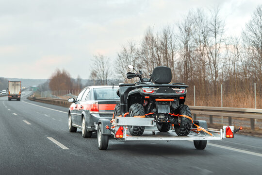 Four-wheeler strapped on trailer behind car