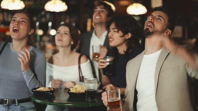 Sports fans react with disappointment to changes in bad luck game. Group of friends hangs out at sports bar, watching teams match, and following progress of game. Video broadcast of match or race is