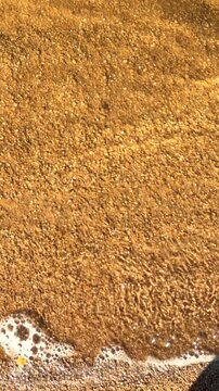 Close up of sandy beach and move small waves and white foam. Natural moving water on Borovoe Lake. Brown yellow sand texture and ripples surface. Calm summer and minimal nature scenery, top view.
