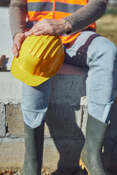 Construction worker working outdoors on a construction site, making a pause and holding a yellow hardhat.