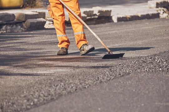Construction worker working on a new asphalt layer on a public street.