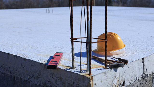 Construction tools and helmet on a cement foundation with iron rebar.