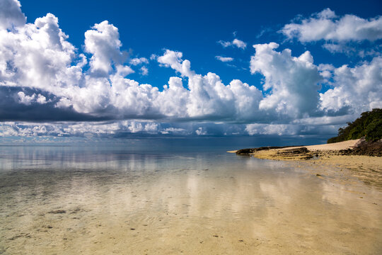 Calm shallow water and sandy shoreline beneath towering clouds at Heron Island on the southern Great Barrier Reef, Queensland, Australia.