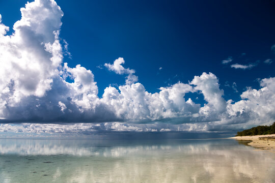 Calm shallow water and sandy shoreline beneath towering clouds at Heron Island on the southern Great Barrier Reef, Queensland, Australia.