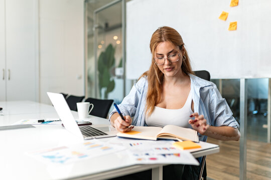 Planning daily schedule. Business notes, Organization and productivity concept. Young businesswoman sitting at the office desk, writing important information in her notebook with a pen.