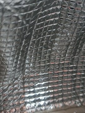 Reflective metallic material with geometric dimples. Light glints off the surface.