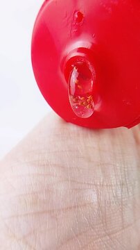 Point of view pouring clear gel liquid with raspberry extract onto hand skin. Liquid dispensing from red product packaging. Isolated white background for beauty skincare concept.