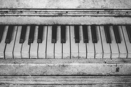 Overhead monochrome view of weathered keys on an old vintage piano with scratched wooden panel texture