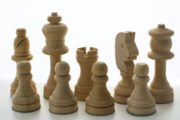 Close up of a set of light wooden chess pieces arranged on a white background © Nazar