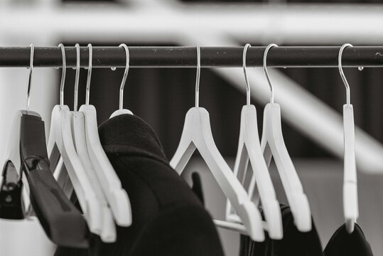 Monochrome close up view of empty white wooden hangers arranged on a black metal clothing rack