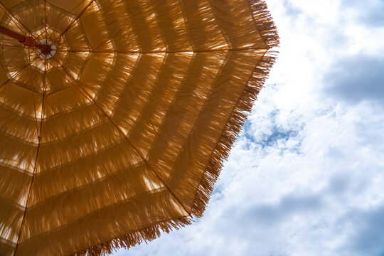 Bright Sunshade Beneath a Blue Sky: A Beautiful View of a Straw Umbrella with Fluffy Clouds in the Background