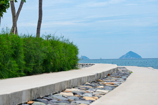 Serene Coastal Pathway Surrounded by Lush Greenery Leading to Tranquil Waters and Distant Islands Under a Clear Sky