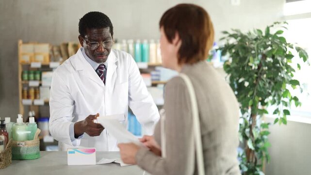In drug store, African man at counter sells medication to customer, offer remedy and consulting about doctors prescription. Everyday life at pharmacy, customer support 