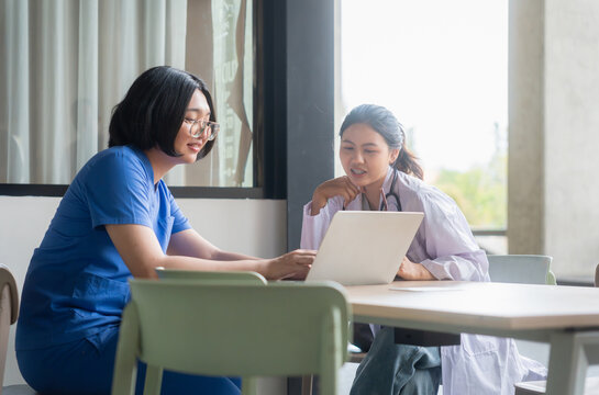 Asian medical staff working with laptop together at hospital desk, doctor and nurse in uniform looking at laptop screen in meeting room, healthcare professionals discussing medical project indoors