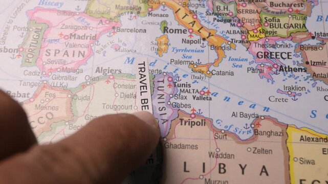 Hand pointing at Travel Begins Here label on Mediterranean map for trip planning
