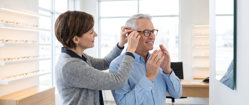 Optometrist adjusts prescription eyeglasses for mature patient, evaluating frame fit, comfort and vision while providing personalized eye care in modern optical clinic.