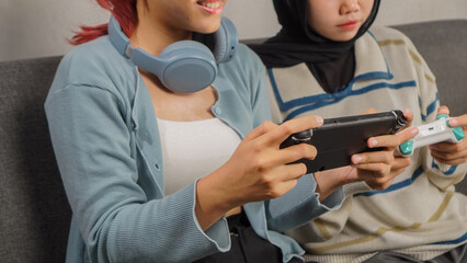 Close up of two young Asian women using console game and joystick, enjoying a shared gaming moment. © ChristyMerry