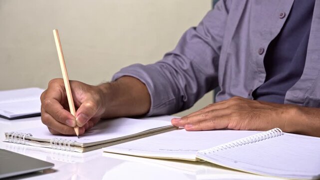Person in grey shirt writing essay in spiral notebook at desk