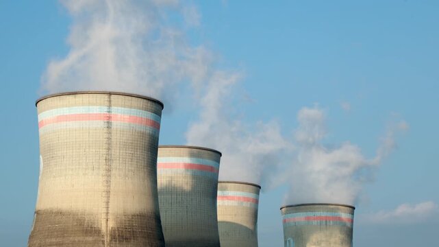 Industrial cooling tower emitting white steam into blue sky