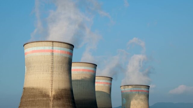 Industrial cooling towers emitting steam against blue sky