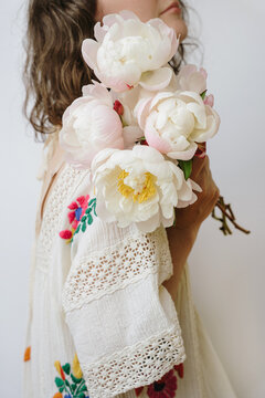 Female In Bohemian Embroidered Dress Holding Blooming Pink Peony Bunch Against White Background