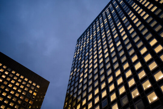 Low angle view of illuminated office towers in La Defense business district in Paris, France at blue hour with dramatic urban geometry