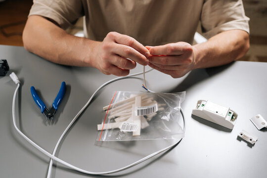 Close-up top view of technician male fixing electrical wire, stripping insulation from cable, performing maintenance, working on home repair or diy technology projects sitting at desk.