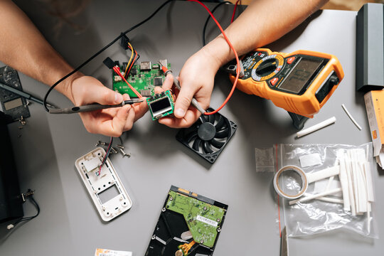 Close-up of technician using multimeter to diagnose electronic circuit board, troubleshooting computer hardware, installing parts, repairing modern digital device, measuring voltage on motherboard.