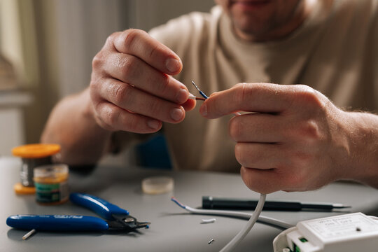 Skilled repairman hands working on electrical wires, stripping insulation and connecting power cable to controller, symbolizing repair, installation and technical support for electronic components.