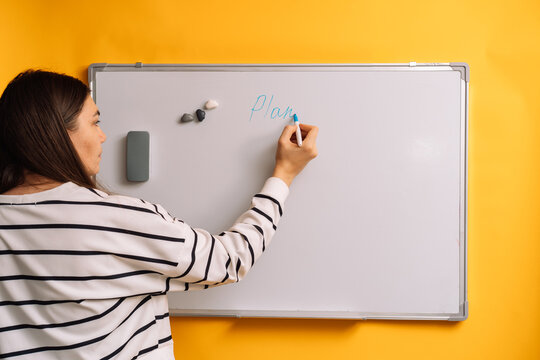 Woman writing Plan on a whiteboard with a blue marker wearing a striped top.