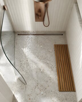 Pale terrazzo wet room floor sloping to a slim linear drain with a curved glass screen