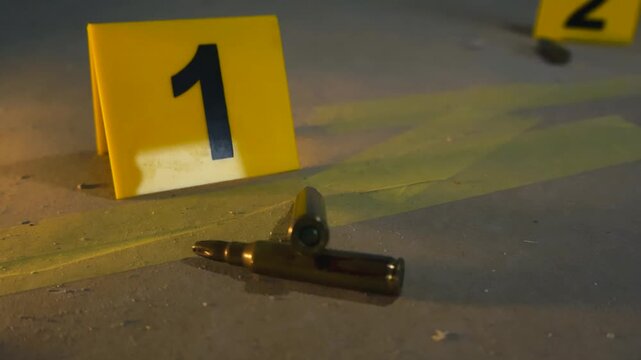 Close up view of bullet casings lying on a concrete floor next to yellow evidence markers at a crime scene, highlighting a criminal investigation and forensic evidence gathering process