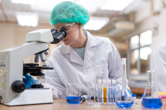 Young female researcher working in the lab, she is examining the samples under a microscope