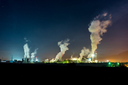 Night view of a massive industrial factory emitting thick smoke into the dark sky, highlighting air pollution and environmental damage.