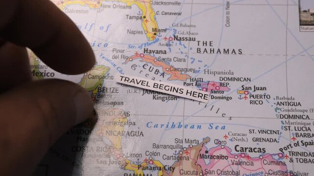 Hand placing travel begins here label on map of Caribbean sea close up