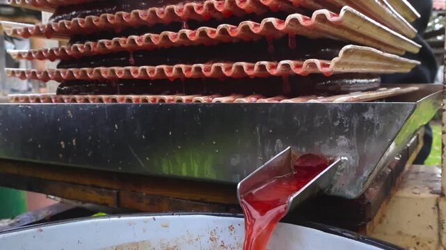Stream of freshly pressed apple and chokeberry juice flowing from a fruit press during the production process. Slow motion captures the vibrant red liquid dripping between the plates