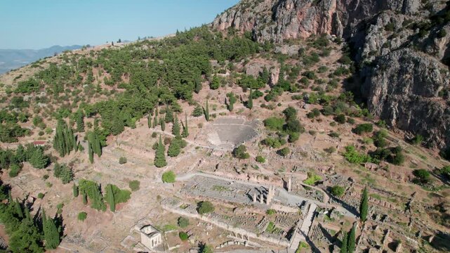 Aerial view of the ancient archaeological site of Delphi with its historic theater and temple ruins nestled on a rocky hillside in Delphi, Greece.