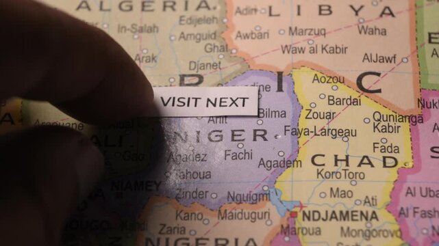 Person placing Visit Next text note on map over Niger country in Africa.